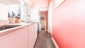 A narrow hallway with a kitchen area on the left, featuring a countertop with utensils and a toaster. The walls are painted in a light color, and there is a framed picture on the right wall. - Lake District cottage with gorgeous views in Beatrix Potter country (Ambleside)