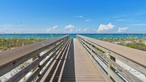 A wooden boardwalk leading to a beach with clear blue water and a few clouds in the sky.