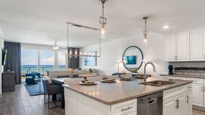 A modern kitchen with a central island, white cabinetry, and a large window overlooking the ocean.