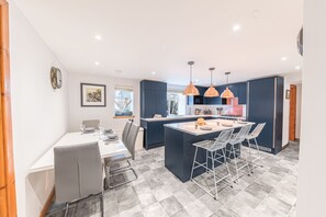 Uma cozinha moderna com ilha central, luminárias pendentes e um espaço de jantar com mesa e cadeiras.