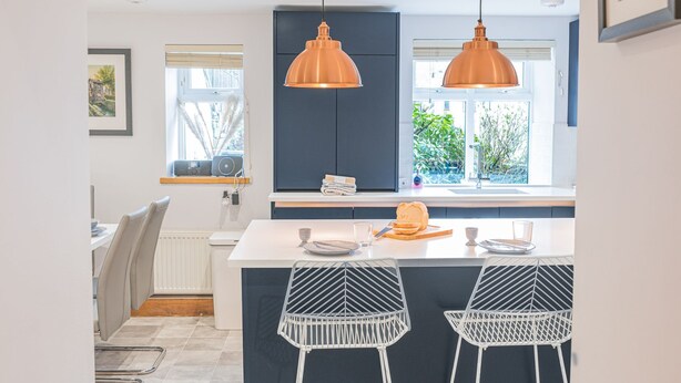 Una cucina moderna con due lampade a sospensione, un'isola centrale con un filone di pane e vista su un'area verde.