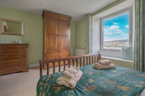 Une chambre à coucher avec un lit, une armoire en bois, une commode et une fenêtre donnant sur la campagne.