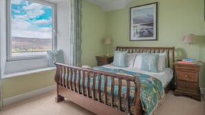 Ein Schlafzimmer mit einem hölzernen Bett, grünen Wänden, einem Fenster mit Ausblick und einem gerahmten Bild an der Wand.