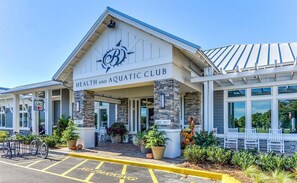 A health and aquatic club with a stone facade, outdoor seating, and a juice box sign.