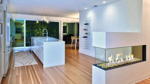 Una cocina moderna con una isla central, una chimenea de vidrio y un comedor con vistas a zonas verdes.