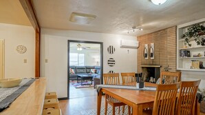 A dining area with a wooden table and chairs, a kitchen with a brick wall, and a living room with a sofa and a coffee table.