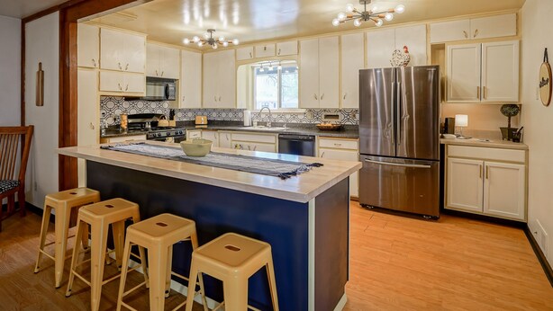 A modern kitchen with a central island, bar stools, stainless steel appliances, and white cabinetry.