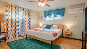 A bedroom with a bed, a ceiling fan, a window with curtains, a nightstand, and an air conditioning unit.