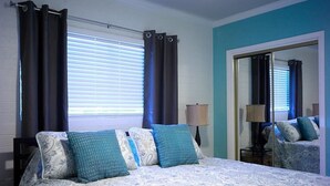 A bedroom with a bed, curtains, a mirror, and a lamp.