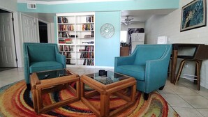A living room with teal armchairs, a coffee table, a bookshelf, and a colorful rug.