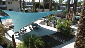 A pool area with a shaded seating area, palm trees, and a stone pathway.
