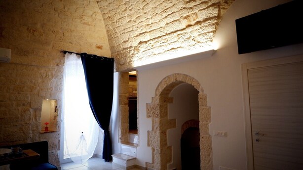 A room with stone walls, a wooden door, and a window with a black curtain.