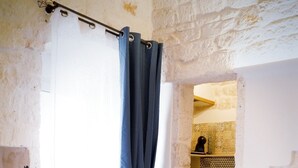 A room with a blue sofa, a wooden coffee table, a curtain, and a view of a bathroom with patterned tiles.