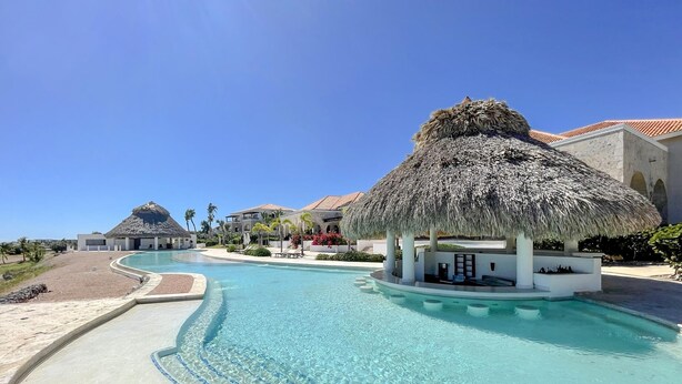 Een resort met een groot zwembad, een gazebopaviljoen met rieten dak en moderne villa's.