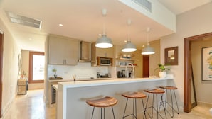 Een moderne keuken met een centraal eiland, barstoelen, hanglampen en een magnetron.