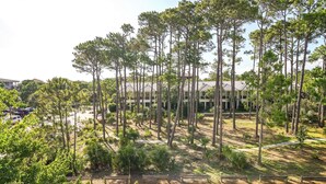 A building surrounded by tall pine trees, with a parking lot and a pathway in the foreground. - Snowbird Specials-2 Minute Walk Private Beach-3 Pools - Gulf Place (Santa Rosa Beach)