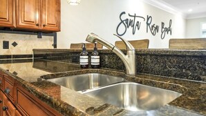 A kitchen with granite countertops, stainless steel sink, wooden cabinets, and a wall sign that reads "Santa Rosa Beach". - Snowbird Specials-2 Minute Walk Private Beach-3 Pools - Gulf Place (Santa Rosa Beach)