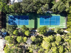 An aerial view of a tennis court surrounded by dense greenery and trees.
