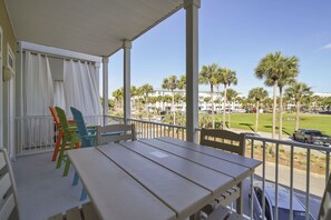 A balcony with a table and chairs, overlooking a parking area with palm trees and a building in the background.