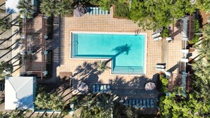 An aerial view of a resort with a rectangular pool, surrounded by palm trees and shaded areas with umbrellas. - Snowbird Specials-2 Minute Walk Private Beach-3 Pools - Gulf Place (Santa Rosa Beach)