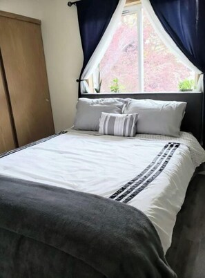 Cozy retreat with a plush bed, a potted plant, and a window with dark curtains.