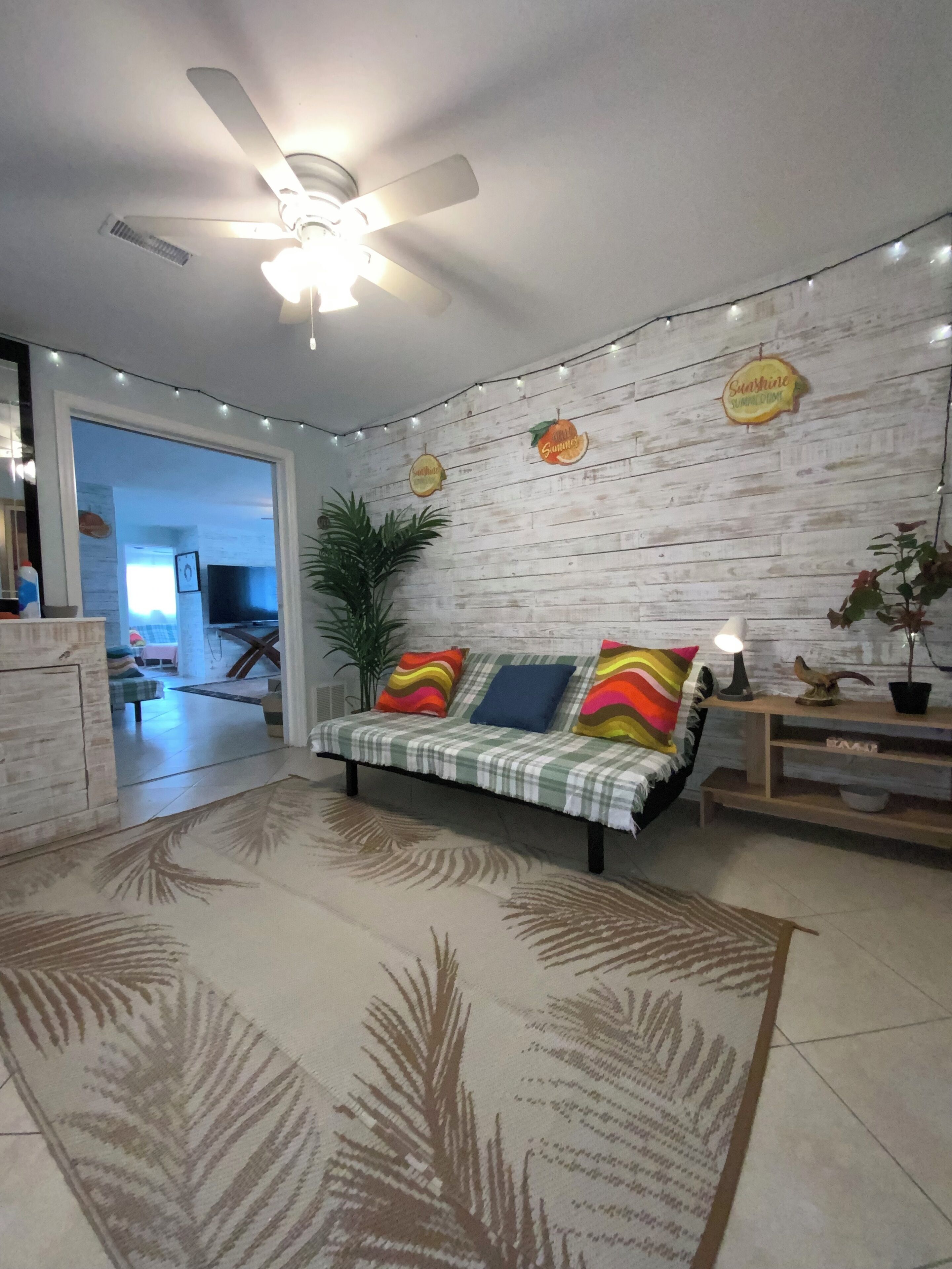A living room with a sofa, a ceiling fan, a plant, and a wall with wooden panels.