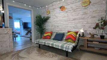A living room with a sofa, a ceiling fan, a plant, and a wall with wooden panels.