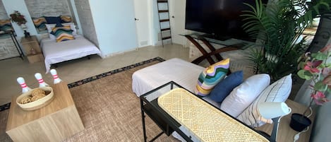 Ein modernes Wohnzimmer mit einer Couch, einem Fernseher, einem Esstisch und einem großen Fenster.
