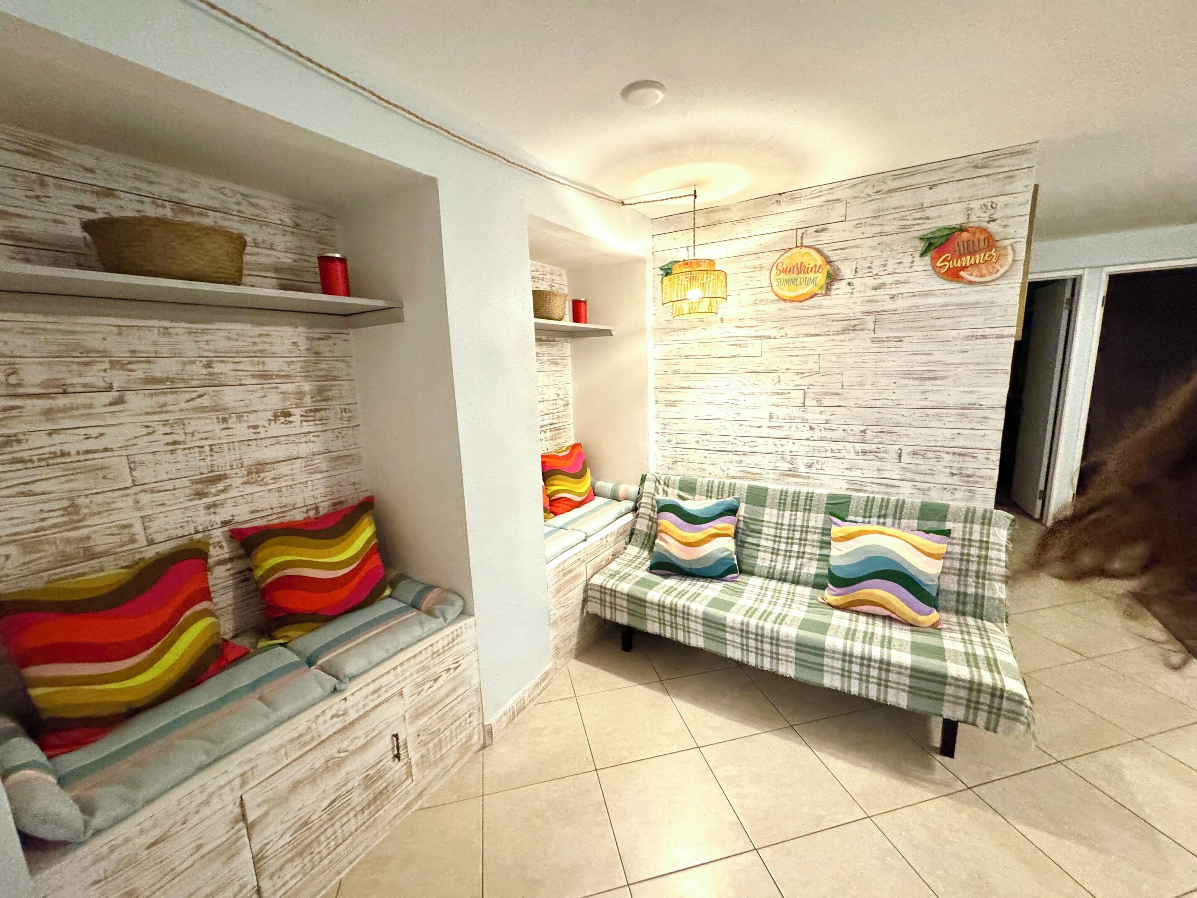 A room with a sofa, a bench, a wall with a wooden texture, and a shelf with items.