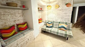 A room with a sofa, a bench, a wall with a wooden texture, and a shelf with items. - MANASOTA BEACH 1 MINUTE AWAY! (Englewood)