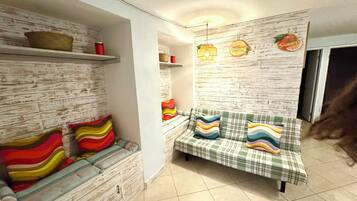 A room with a sofa, a bench, a wall with a wooden texture, and a shelf with items.