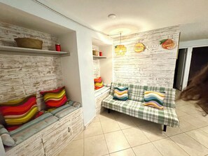Una habitación con sofá, un banco, una pared con textura de madera y una estantería con objetos.