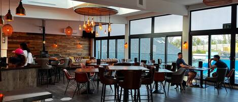 A modern restaurant with a wooden interior, large windows, and a pool view.