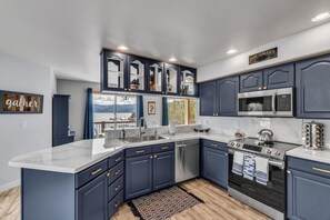 Una cocina moderna con armarios azul oscuro, una isla grande, electrodomésticos de acero inoxidable y vistas al exterior.