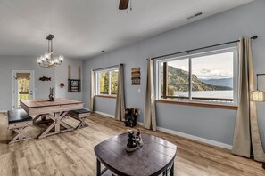 Habitación amplia con un gran ventanal que ofrece vistas a la montaña, una mesa de comedor de madera y una araña.