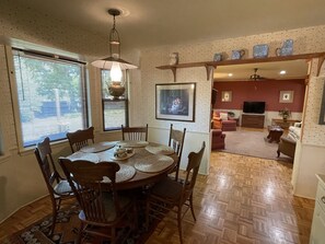 A dining area with a round table and chairs, a hanging light fixture, and a view of the living room through an open doorway.