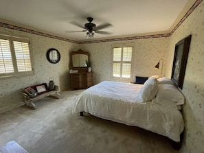 A bedroom with a bed, dresser, vanity, and a ceiling fan.