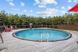 A rectangular swimming pool with a wooden deck, surrounded by a wooden fence and trees.