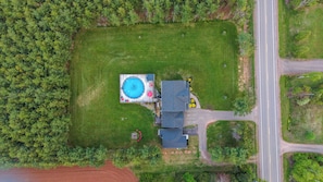 Oversigtsbillede af en ejendom med swimmingpool, hus og vej.