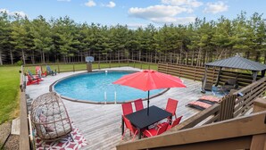 Une terrasse en bois avec une piscine, des chaises rouges, une table et un kiosque.