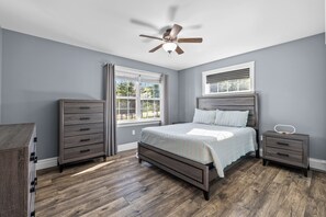 A bedroom with a bed, a nightstand, a dresser, a ceiling fan, and a window.