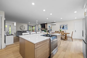 A modern kitchen with a central island, built-in oven, and a dining area with a table and chairs.