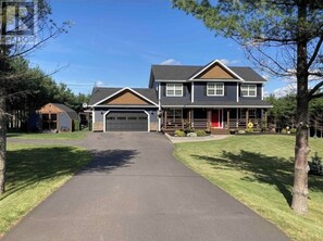 Stunning two-story home with a central entrance and gabled roof, set amidst lush greenery.
