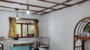 A compact kitchen with a central island, a sink, and a stove. There are two bar stools and a window with patterned curtains. - Perfect location for low budget travel (Quepos)