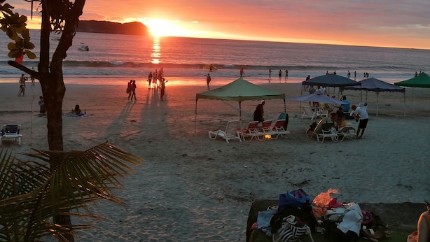 A beach scene with people walking, tents, and beach chairs. - Perfect location for low budget travel (Quepos)