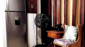 A compact room with a refrigerator, a fan, and a wooden chair with a patterned cushion. - Perfect location for low budget travel (Quepos)