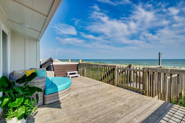A wooden deck with outdoor seating, overlooking a beach.