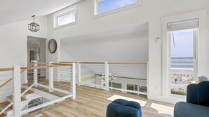Tilava huone, jossa on puulattia, parveke, jolta avautuu näkymä rannalle, sekä moderni kattokruunu.