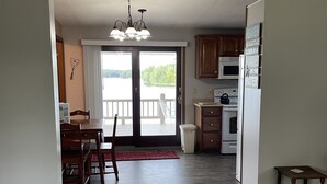 Un vaste espace de vie comprenant un coin repas avec table et chaises, une cuisine équipée d’appareils modernes et une grande porte-fenêtre coulissante donnant sur un balcon avec vue sur un lac.