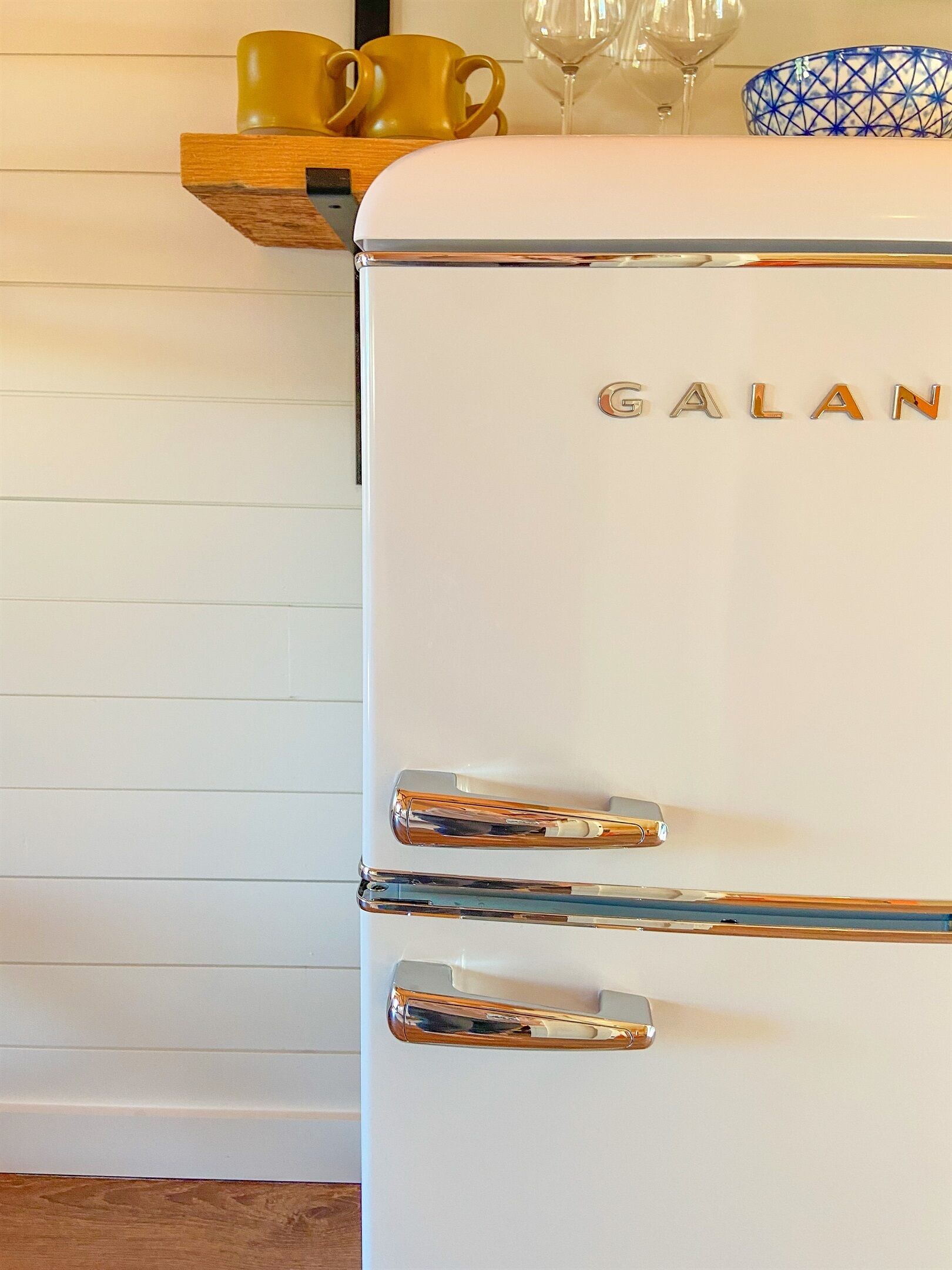 A white Galan refrigerator with chrome handles and a blue patterned bowl on top.
